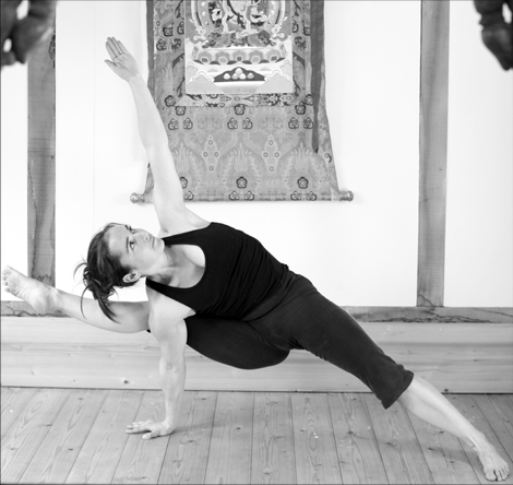 Black and white: an extended side-arm pose in front of a wall hung with a large patterned thangka